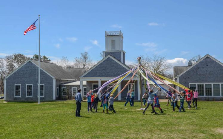 grassy field with pole that is circled by children with ribbons attached to pole to dance and weave 